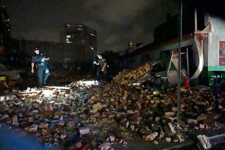 New Orleans Police detectives Adam Buckner, left, and Alexander Reiter, look over debris from a building that collapsed during Hurricane Ida in New Orleans, Monday, Aug. 30, 2021. Hurricane Ida knocked out power to all of New Orleans and inundated coastal Louisiana communities on a deadly path through the Gulf Coast that is still unfolding and promises more destruction. (AP Photo/Gerald Herbert)