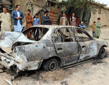 Locals view a vehicle damaged by a rocket attack in Kabul