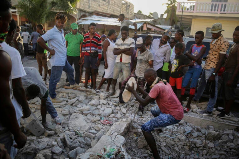 A man digs with a stone through the rubble of a house destroyed by the earthquake in Les Cayes