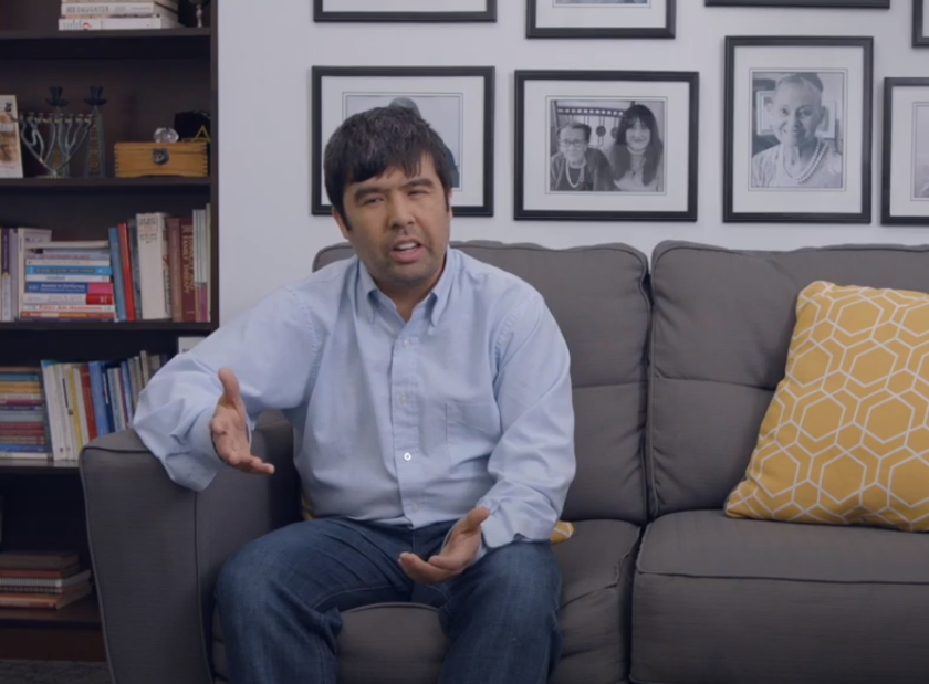 Sadiq gestures while sitting on a couch