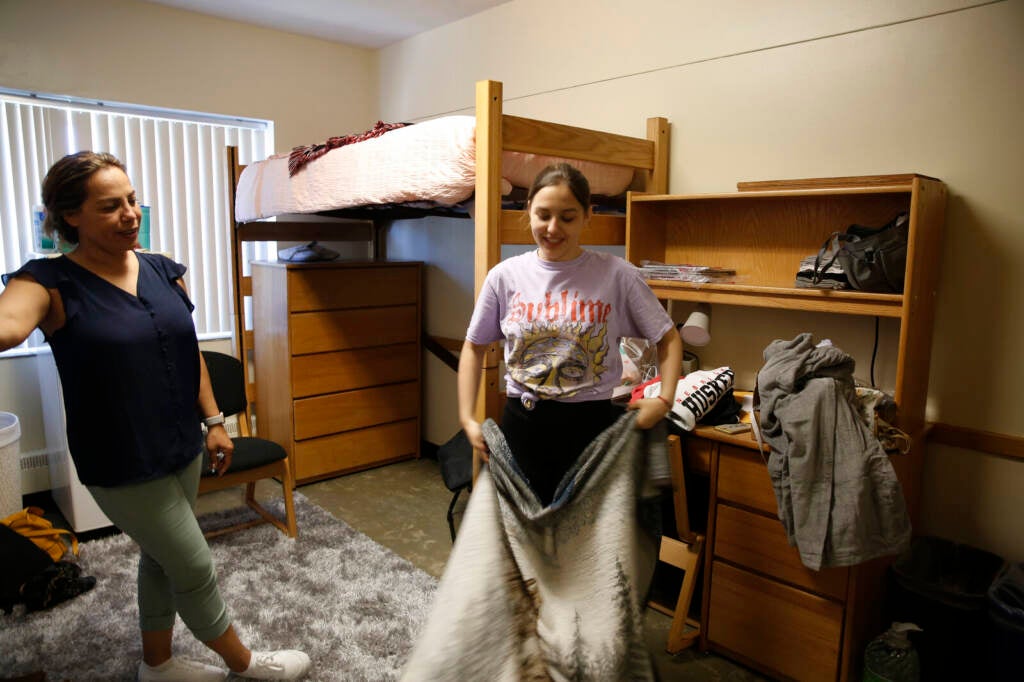 Kitana Bernth holds up a blanket in her dorm room, with her mom standing next to her