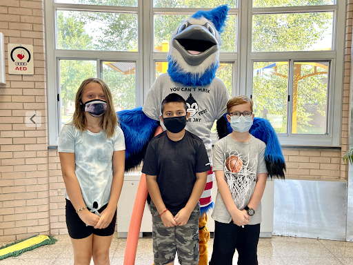 Three students wearing masks stand in front of a mascot