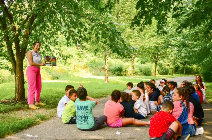 A group of children sitting outside as a teacher reads to them