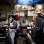 A kitchen worker wears a surgical mask and gloves as he prepares food