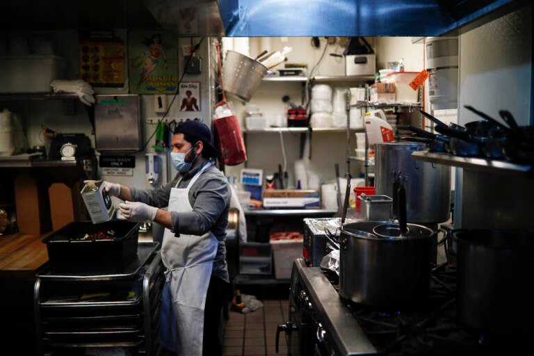 A kitchen worker wears a surgical mask and gloves as he prepares food