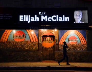 FILE - In this Aug. 24, 2020, file photo, a man walks past a display showing an image of Elijah McClain outside Laugh Factory during a candlelight vigil for McClain in Los Angeles.   Colorado’s attorney general said Wednesday, Sept. 1, 2021 that a grand jury indicted three officers and two paramedics in the death of Elijah McClain, a Black man who was put in a chokehold and injected with a powerful sedative two years ago in suburban Denver. (AP Photo/Jae C. Hong, File)