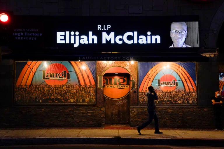 FILE - In this Aug. 24, 2020, file photo, a man walks past a display showing an image of Elijah McClain outside Laugh Factory during a candlelight vigil for McClain in Los Angeles.   Colorado’s attorney general said Wednesday, Sept. 1, 2021 that a grand jury indicted three officers and two paramedics in the death of Elijah McClain, a Black man who was put in a chokehold and injected with a powerful sedative two years ago in suburban Denver. (AP Photo/Jae C. Hong, File)