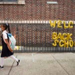 FILE - In this Sept. 13, 2021, file photo, a girl passes a 'Welcome Back to School' sign as she arrives for the first day of class. (AP Photo/Mark Lennihan, File)