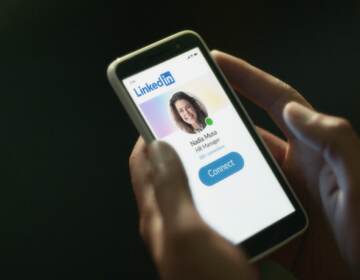 A person holds a phone whose screen shows the LinkedIn app.