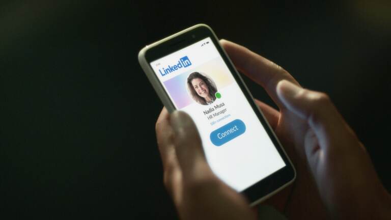 A person holds a phone whose screen shows the LinkedIn app.