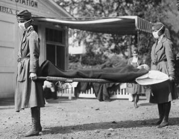 Two people hold either ends of a gurney during the 1918 pandemic