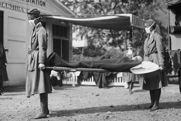 Two people hold either ends of a gurney during the 1918 pandemic