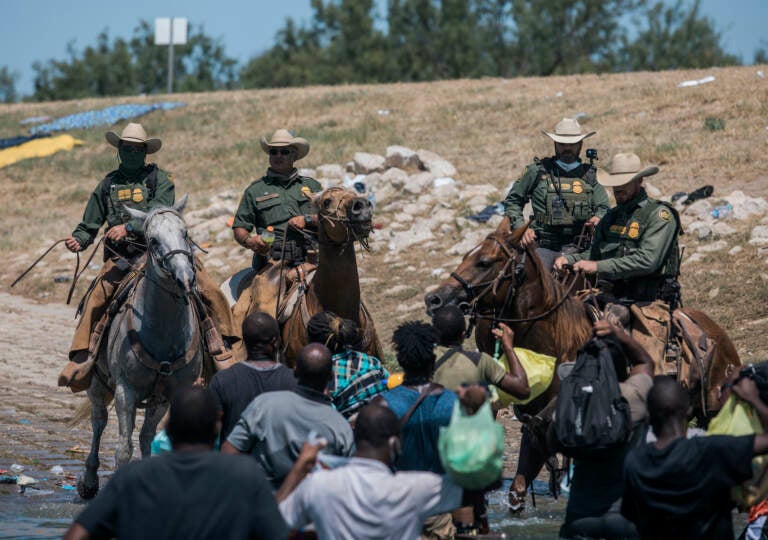 U.S. border patrol officers are seen on horses, with Haitian migrants pictured crossing the Rio Grande below