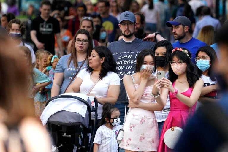 People wait to cross the street, some wearing face masks