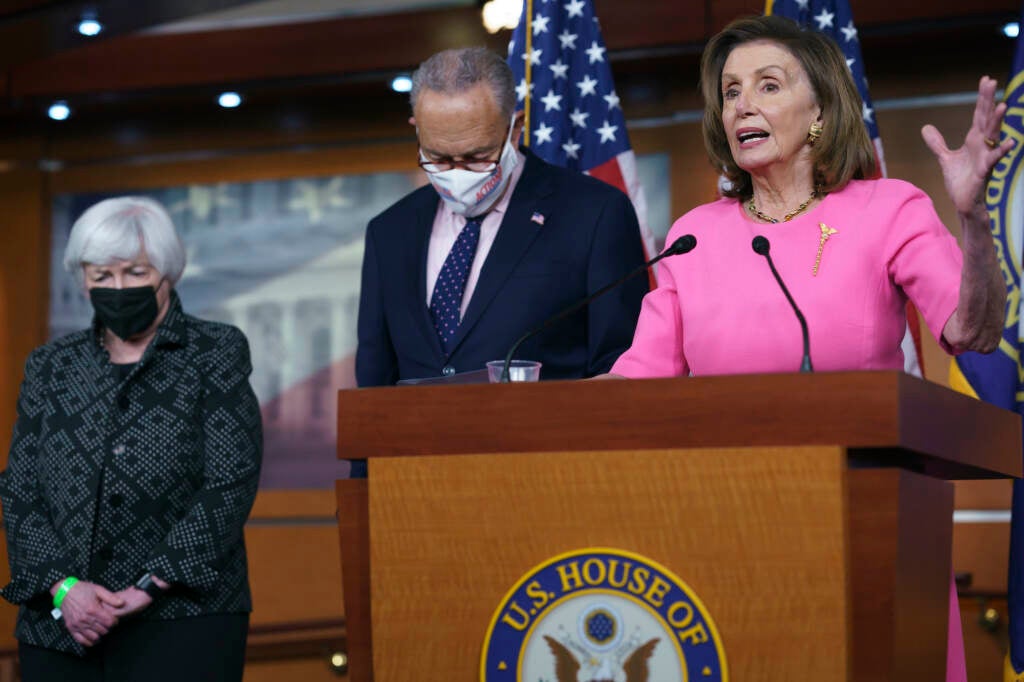Nancy Pelosi stands at a podium, with Chuck Schumer and Janet Yellen standing to her right