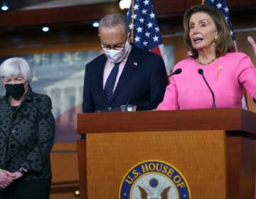 Nancy Pelosi stands at a podium, with Chuck Schumer and Janet Yellen standing to her right