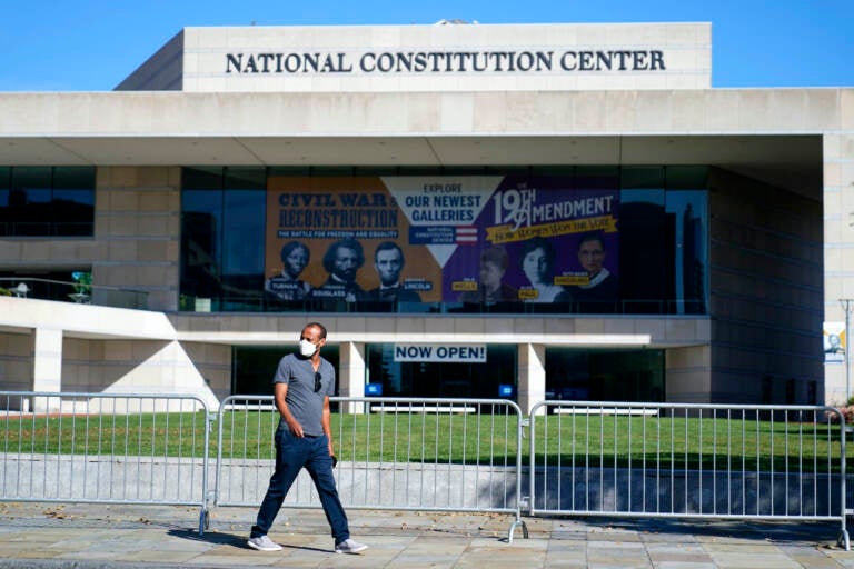 A man walks past the National Constitution Center while wearing a mask