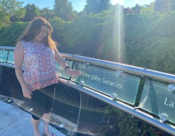 Ellen Saracini touches a memorial plaque for her husband Victor that is illuminated by late afternoon sunlight. Victor, who piloted one of the doomed planes before being killed by terrorists, is one of 2,973 victims of the terror attacks remembered at the Garden of Reflection. (Brett Sholtis / WITF)