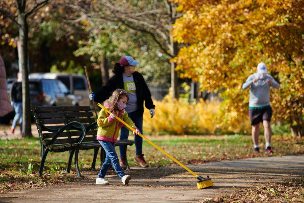 A young girl pushes leaves with a broom at a Philly park