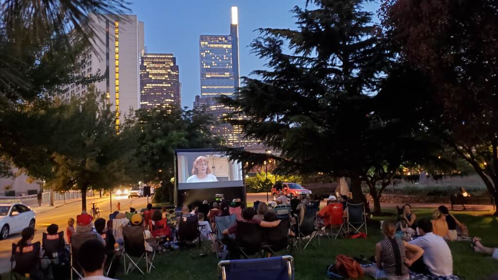 People sit on a park lawn to watch a movie on a projector screen