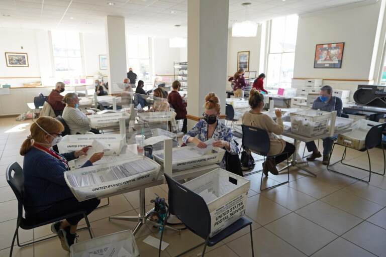 People sit at tables in a room with ballots from the 2020 election