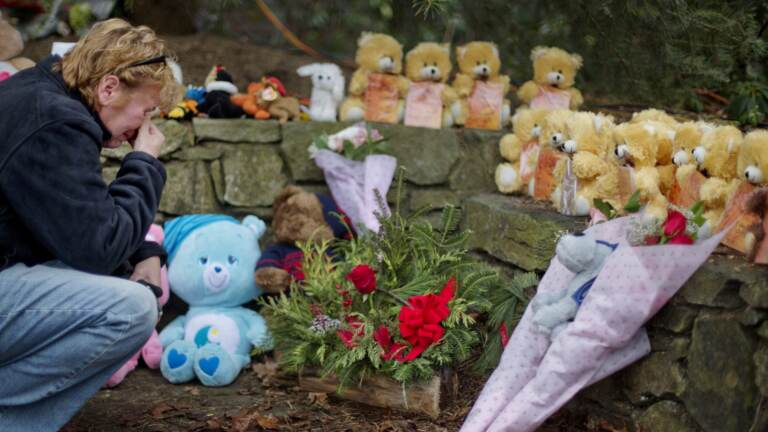 A mourner kneels beside 26 teddy bears