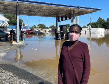 Andrienne Dolley stands in front of a gas station surrounded by floodwaters