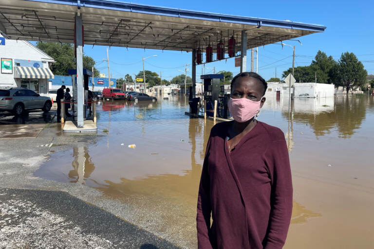 Andrienne Dolley stands in front of a gas station surrounded by floodwaters