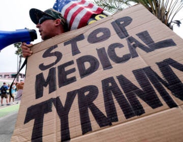 An anti-vaccination protester holds a sign and a flag as he takes part in a rally against Covid-19 vaccine mandates, in Santa Monica, California, on August 29, 2021. (Photo by RINGO CHIU / AFP) (Photo by RINGO CHIU/AFP via Getty Images)