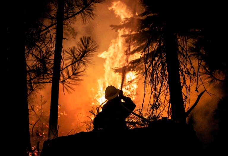 A firefighter with the U.S. Forest Service protects the Strawberry General Store on Highway 50 in El Dorado County after a backfire was set, Saturday, Aug. 28, 2021, against the advancing Caldor Fire