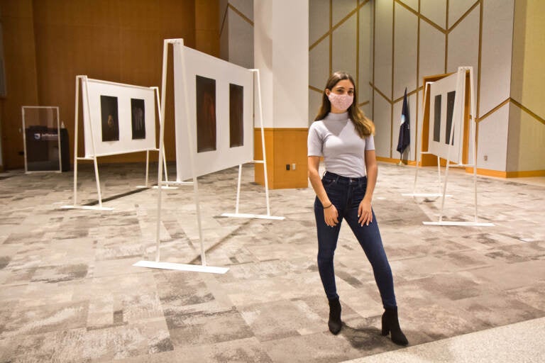 Katherine Cambareri, a graduate with a masters degree in public health from Jefferson College of Population Health, stands with her photographs of clothes worn by survivors of sexual violence at her exhibit at Eakins Lounge at Jefferson Alumni Hall on October 6, 2021. (Kimberly Paynter/WHYY)