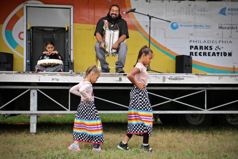 Kai'Lyn Ellis, 5, and her sister, Li'Ana Ellis, 10, members of the Nanticoke Lenape tribe, perform a toe dance while their father, Tyron Ellis chants at Philadelphia's Indigenous Peoples Day celebration at Penn Treaty Park. (Emma Lee/WHYY)