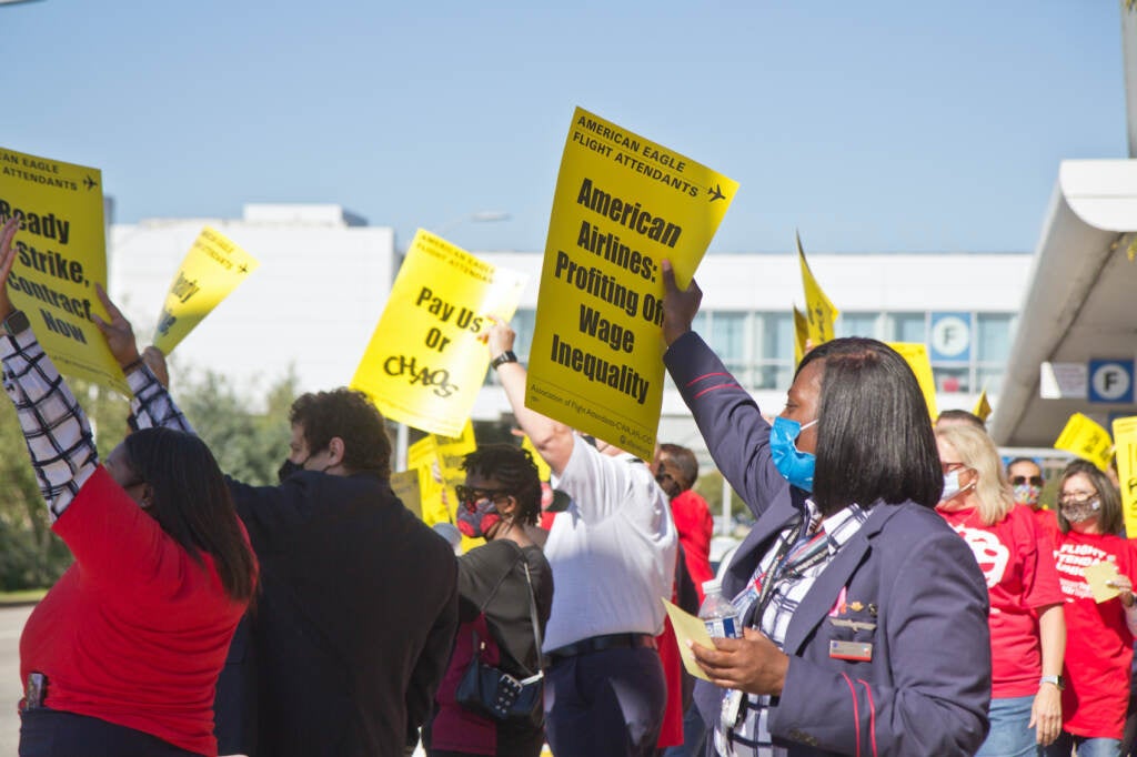 Workers hold up yellow signs at a protest outside PHL Airport