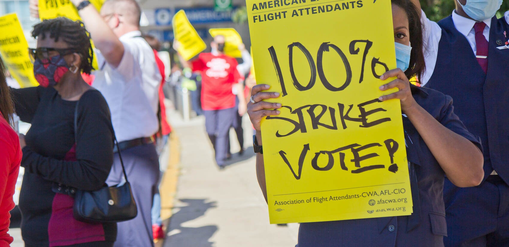 Workers hold up yellow signs at a protest outside PHL Airport
