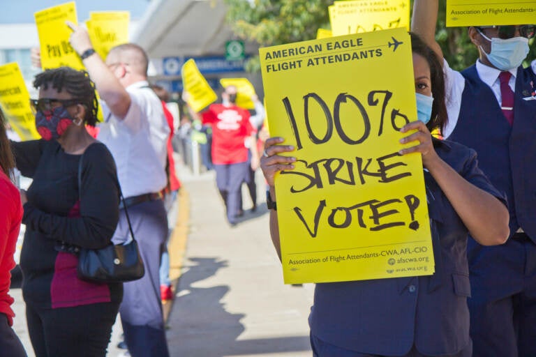 Workers hold up yellow signs at a protest outside PHL Airport