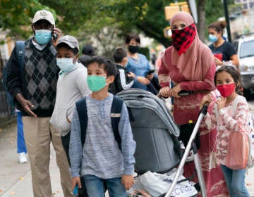 Parents stand with their kids outside, all while wearing face masks