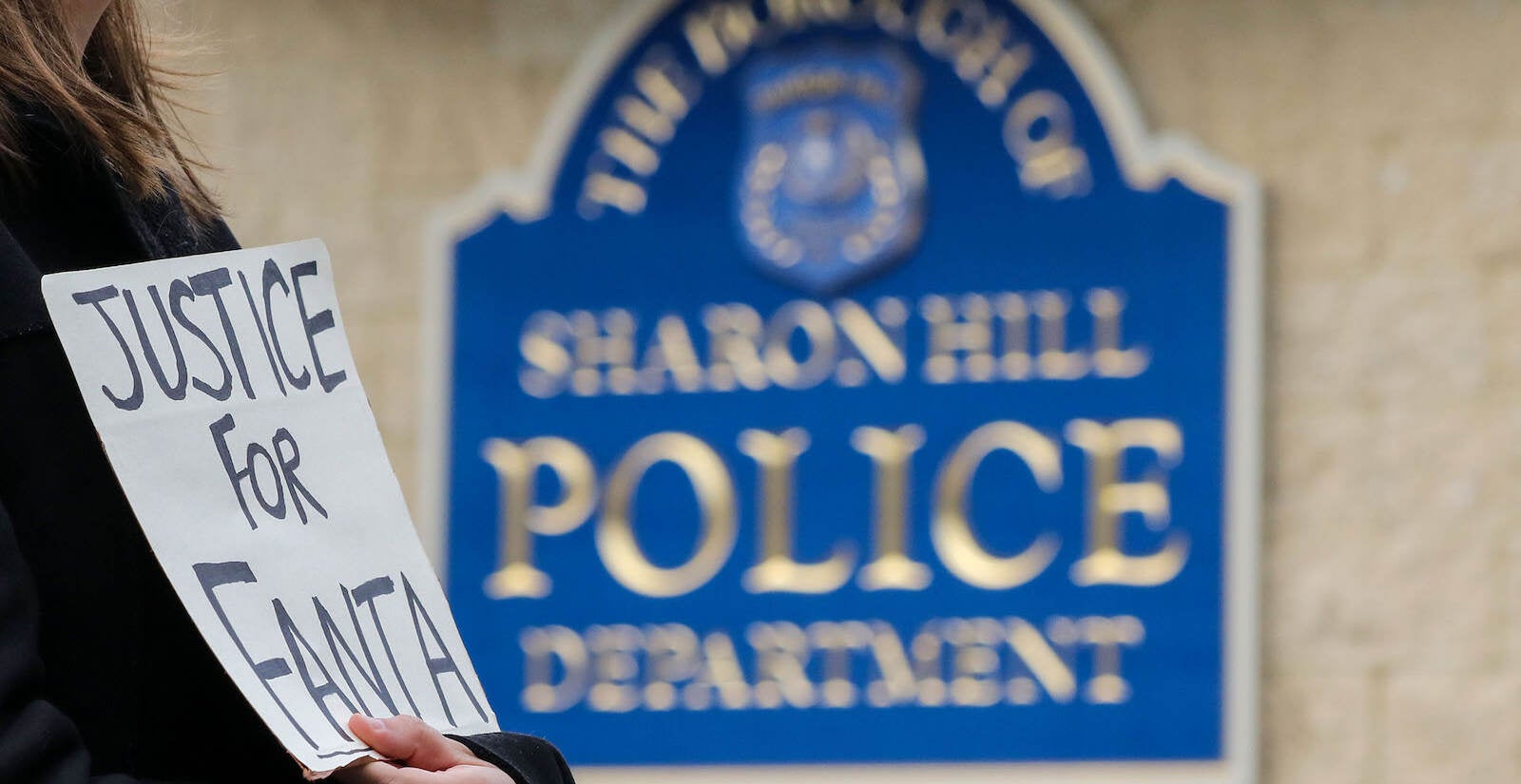 A person holds a sign that reads Justice for Fanta in front of a sign that reads Sharon Hill Police Department.