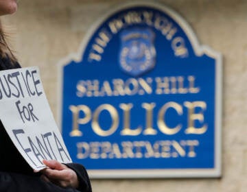 A person holds a sign that reads Justice for Fanta in front of a sign that reads Sharon Hill Police Department.