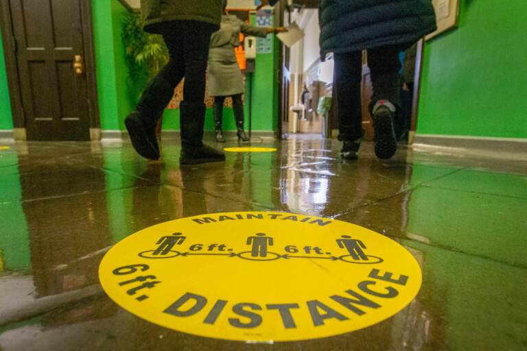 A marker on the floor of a school hallway reminds students to physically distance.