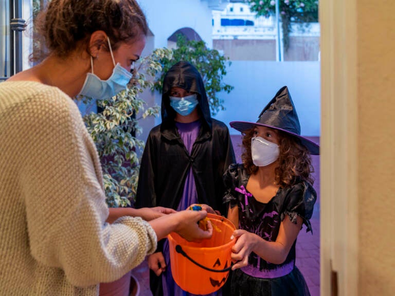 Children dressed in halloween costumes, while wearing face masks, trick-or-treating