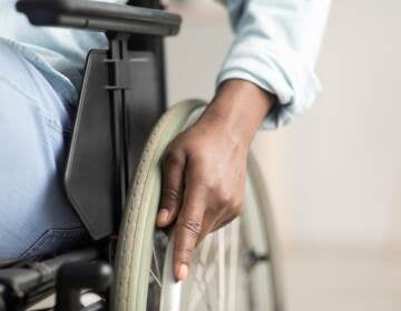 Man controlling equipment, health care in clinic and support of invalid human. Middle aged african american male disabled in wheelchair. Selective focus on hand on wheel, close up, cropped, free space