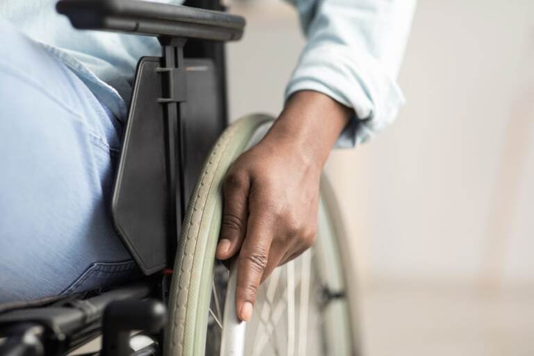 Man controlling equipment, health care in clinic and support of invalid human. Middle aged african american male disabled in wheelchair. Selective focus on hand on wheel, close up, cropped, free space