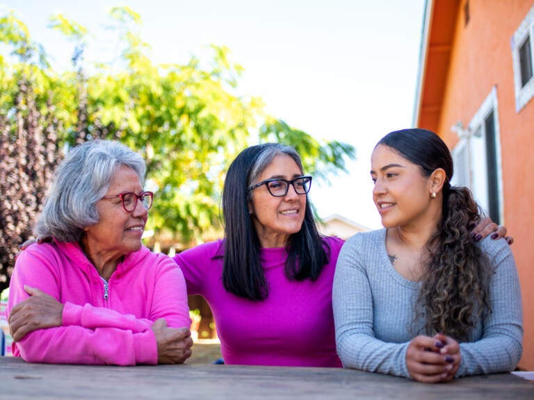 Three generations, (from left to right) grandmother Genoveva Calloway, daughter Petra Gonzales, and granddaughter Vanesa Quintero sit together in their shared backyard in San Pablo on Nov. 3, 2021. (Beth LaBerge/KQED)