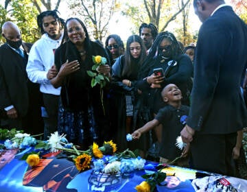 On Nov. 8, at the Sunset Memorial Park Cemetery in Pennsauken, Jassan Lindsey's paternal grandmother, Alma Lindsey, talks about how much her grandson meant to her at his casket; at right, Jassan's younger brother, Kason Lindsey, 4 — too young to comprehend the loss — holds a flower. (April Saul for WHYY)