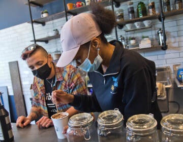 Kim Paulus, general manager of Stomping Grounds Cafe in West Philadelphia and Workforce Development Instructor at Youthbuild Charter High School (left), teaches senior Nyasia Flowers (right) to create a design on a mocha drink