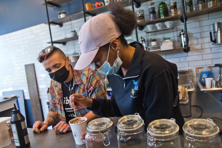 Kim Paulus, general manager of Stomping Grounds Cafe in West Philadelphia and Workforce Development Instructor at Youthbuild Charter High School (left), teaches senior Nyasia Flowers (right) to create a design on a mocha drink