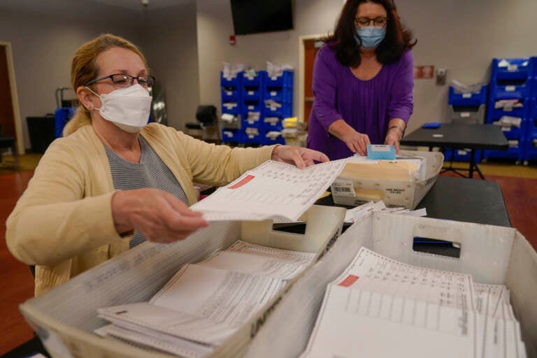 Board worker Ann Carlette, left, process and double-check mail-in ballots