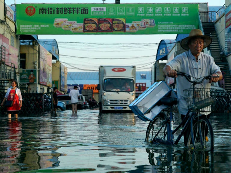 A man carries goods on his bicycle through floodwaters in China