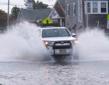 This Oct. 11, 2019 photo shows a car kicking up spray while driving through a flooded street in Bay Head, N.J. Bay Head is moving forward with its own proposed solutions to back bay flooding in response to 