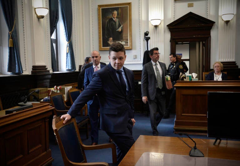 Kyle Rittenhouse, center, pulls out his chair for a meeting Judge Bruce Schroeder called during his trial at the Kenosha County Courthouse in Kenosha, Wis., on Thursday, Nov. 18, 2021